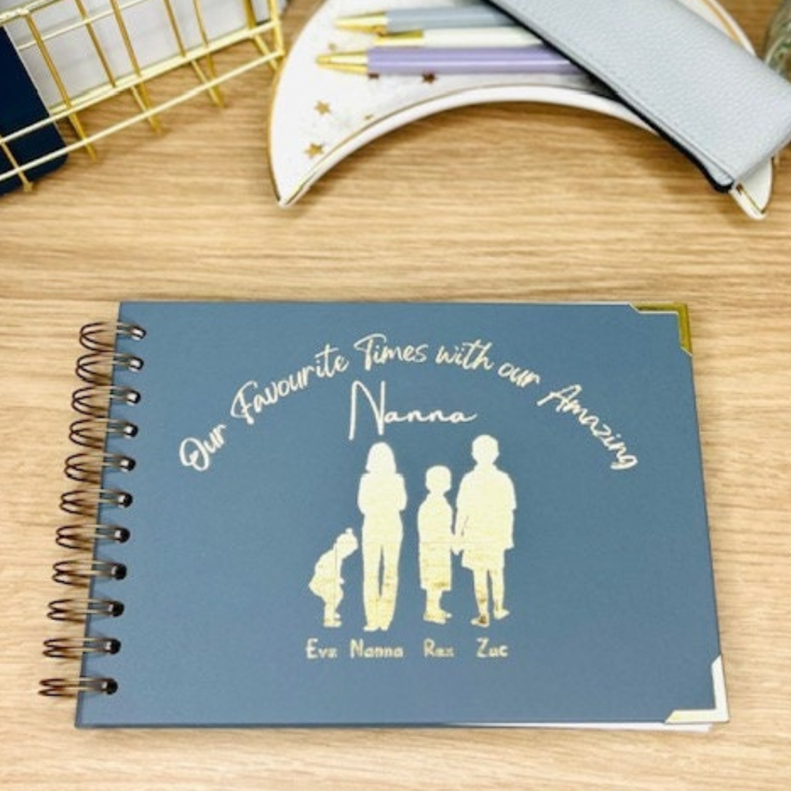 An A5 memory book cover with the words 'Our Favourite Times with our Amazing Nanna' with the silhouettes of a ladie with three different size children with their names underneath. All in gold foil