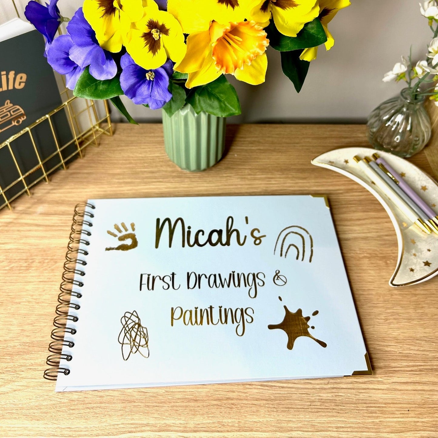 An A4 memory book in Ice Blue that says 'Michah's first drawings and paintings with a paint splodge, scribbles and a hand print all in gold foil