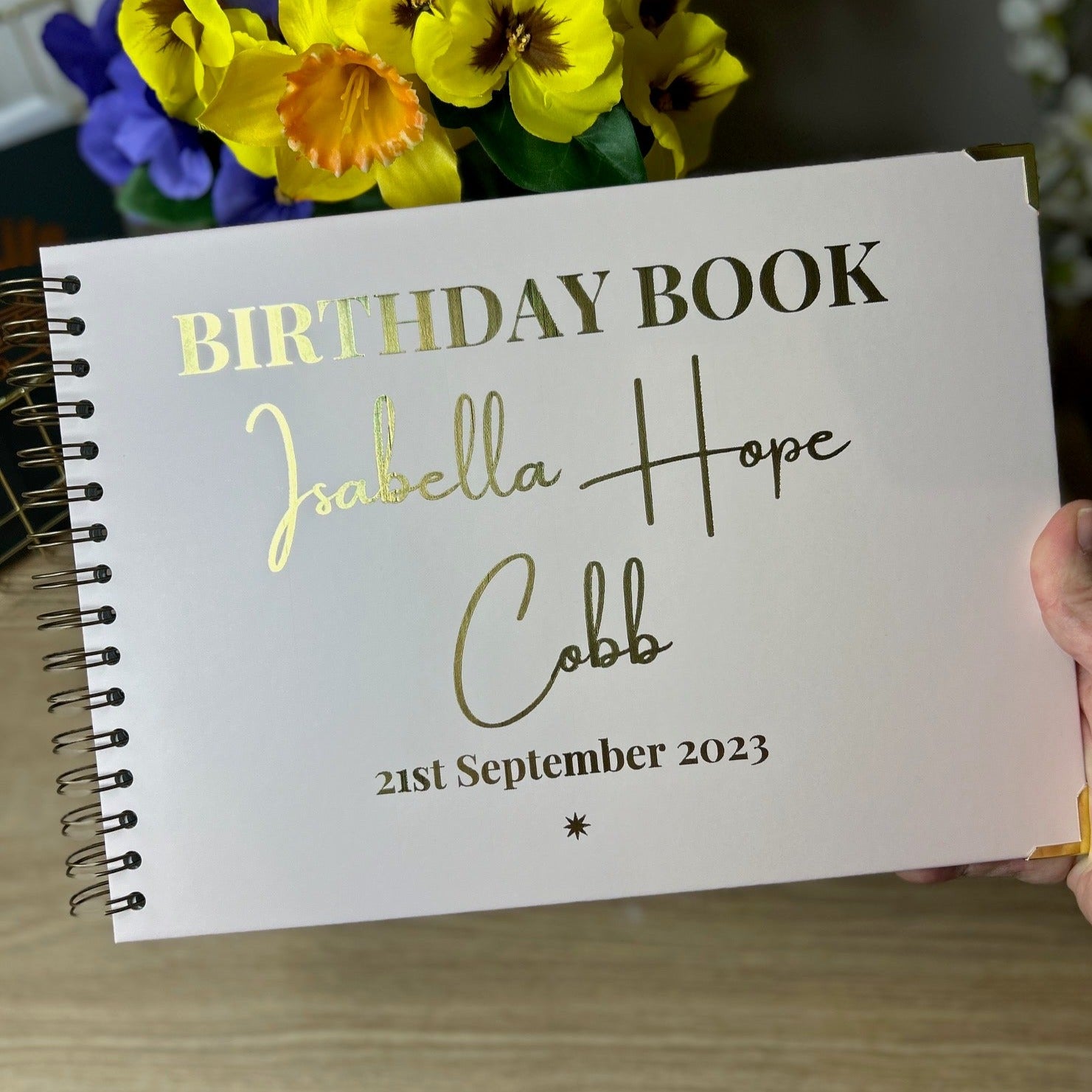 An A4 memory book in stone colour that says 'Birthday Book Isabella Hope Cobb 21st September 2023' in gold foil