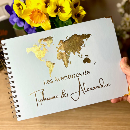 An A4 memory book in blue /grey with a map of the world and the words 'Les Adventures de Tiphaine and Alexandre' All in gold foil' all in gold foil