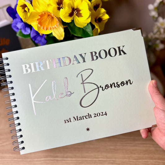 A peppermint coloured A4 book that says 'Birthday Book Kaleb Bronson 1st March 2024' in silver foil