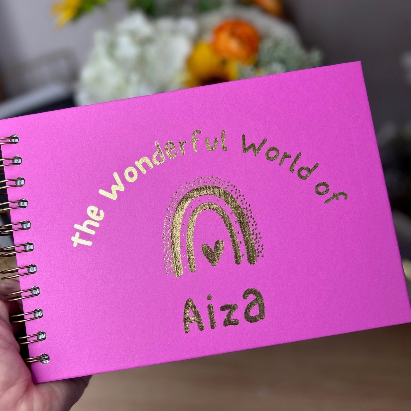 An A5 memory book in Hot Pink that says 'The wonderful world of Aiza with a rainbow all in gold foil