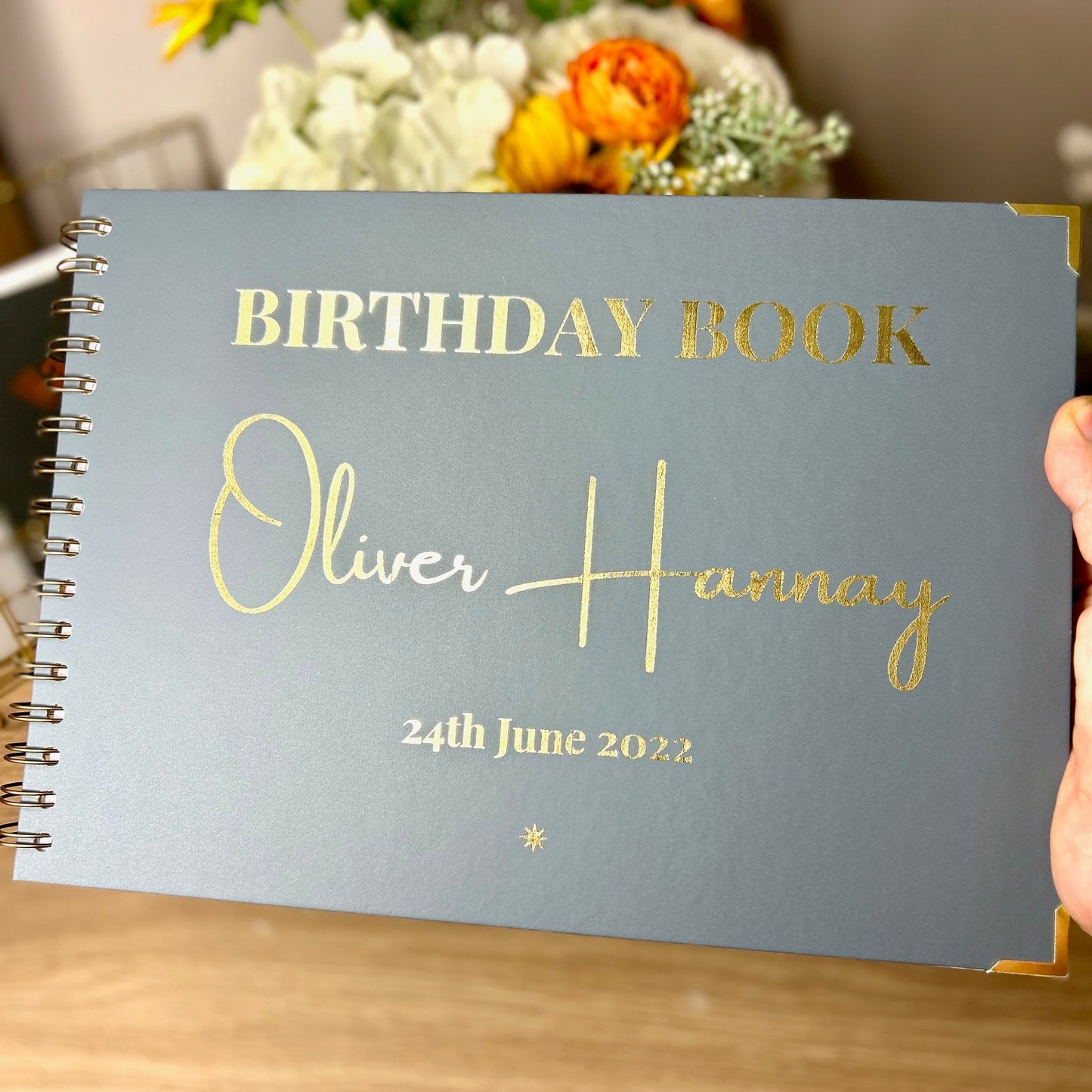 A blue grey memory book with the words 'Birthday Book Oliver Hannay 24th June 2022' in gold foil