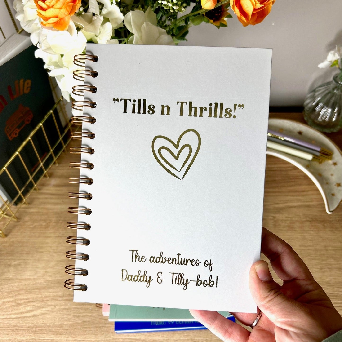 A hardback A5 notebook in Light grey that says 'Tills and thrills - the adventures of Daddy and Tilly-bob' all in gold foil