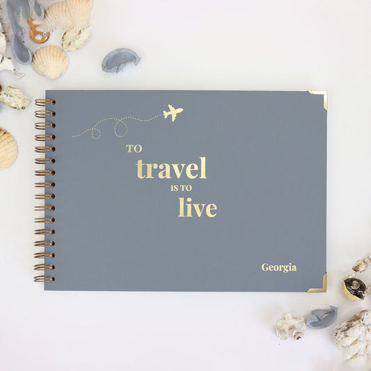 An A4 Memory Book in blue/grey that says 'To travel is to live' with the name Georgia in the bottom corner and an image of an aeroplane at the top, all in gold foil.
