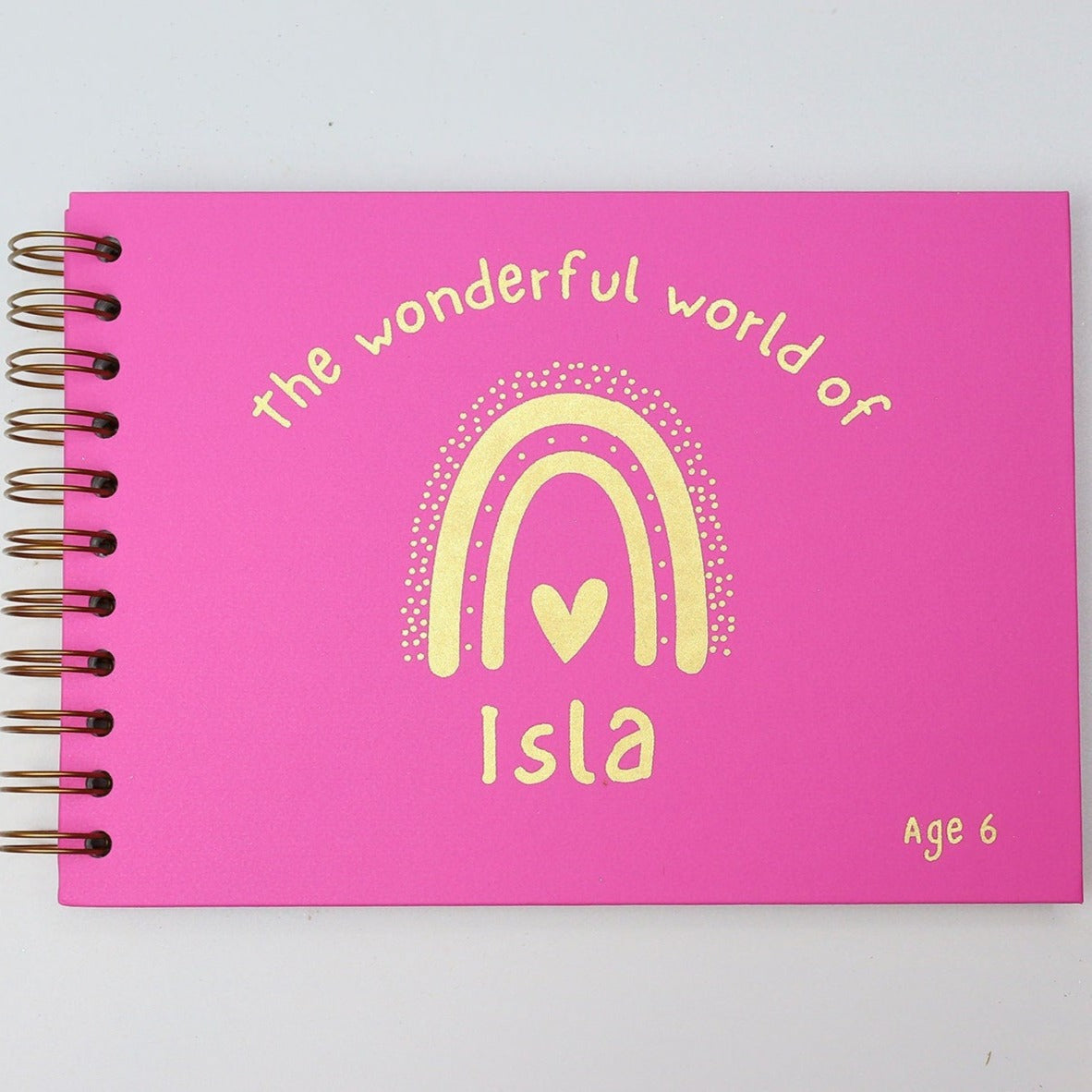 An A5 memory book in Hot Pink that says 'The wonderful world of Isla with a rainbow all in gold foil