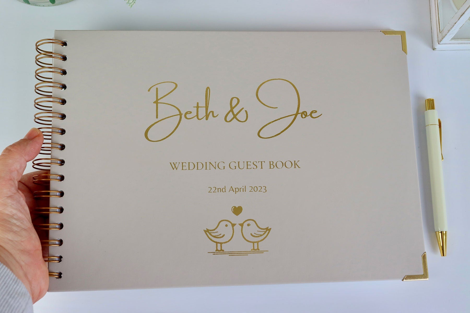 An A4 memory book in stone that says 'Beth and Joe' with 'wedding Guest Book' a date underneath and an image of two love birds kissing all in gold foil