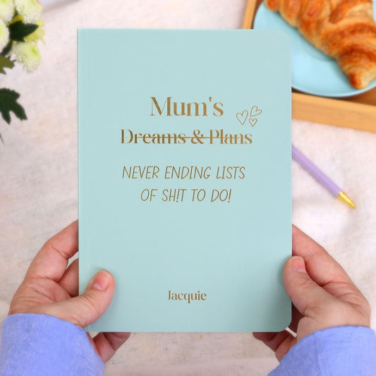 An A5 softback notebook in Sage with the words 'Mum's 9dreams and plans which is crossed out) Never ending lists of shit to do' with the name Jaquie at the bottom all in gold foil