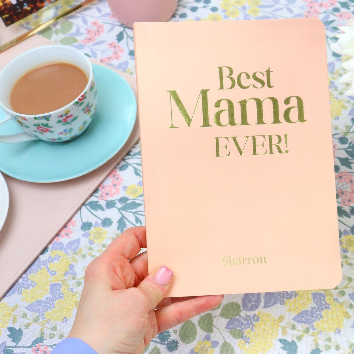 An A5 softback notebook in powder pink that says 'Best Mama Ever' with the name Sharron at the bottom all in gold foil