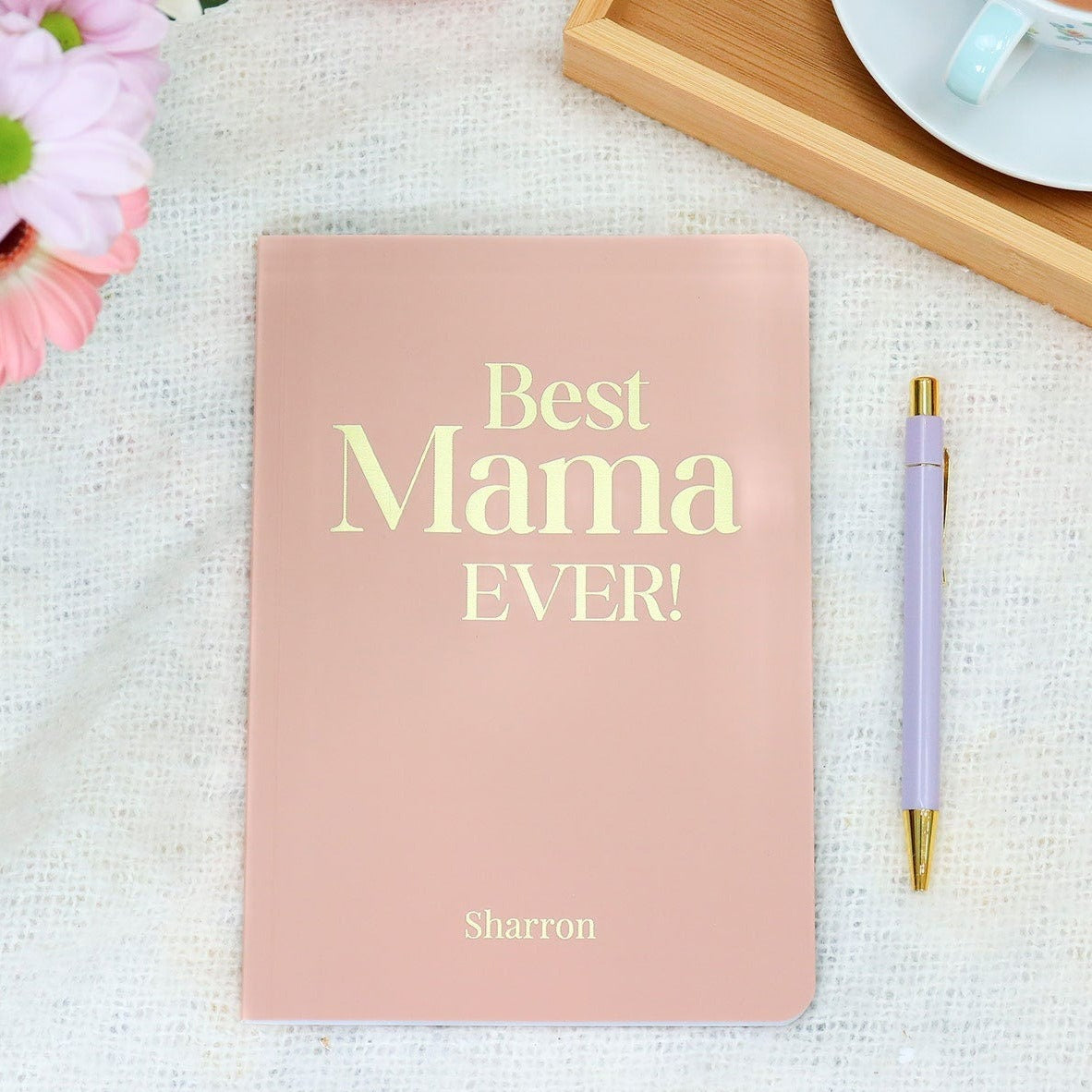 An A5 softback notebook in powder pink that says 'Best Mama Ever' with the name Sharron at the bottom all in gold foil