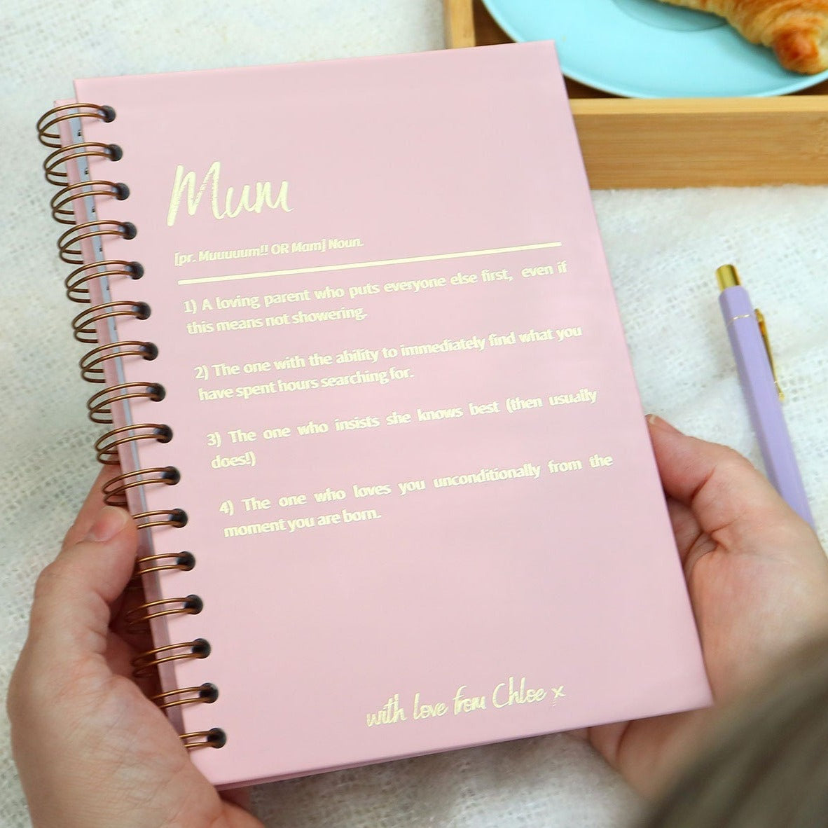 An A5 hardback notebook in powder pink that has 'Mum' at the top with a dictionary style definition underneath all in gold foil