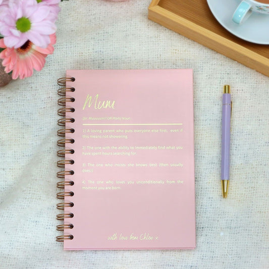 An A5 hardback notebook in powder pink that has 'Mum' at the top with a dictionary style definition underneath all in gold foil