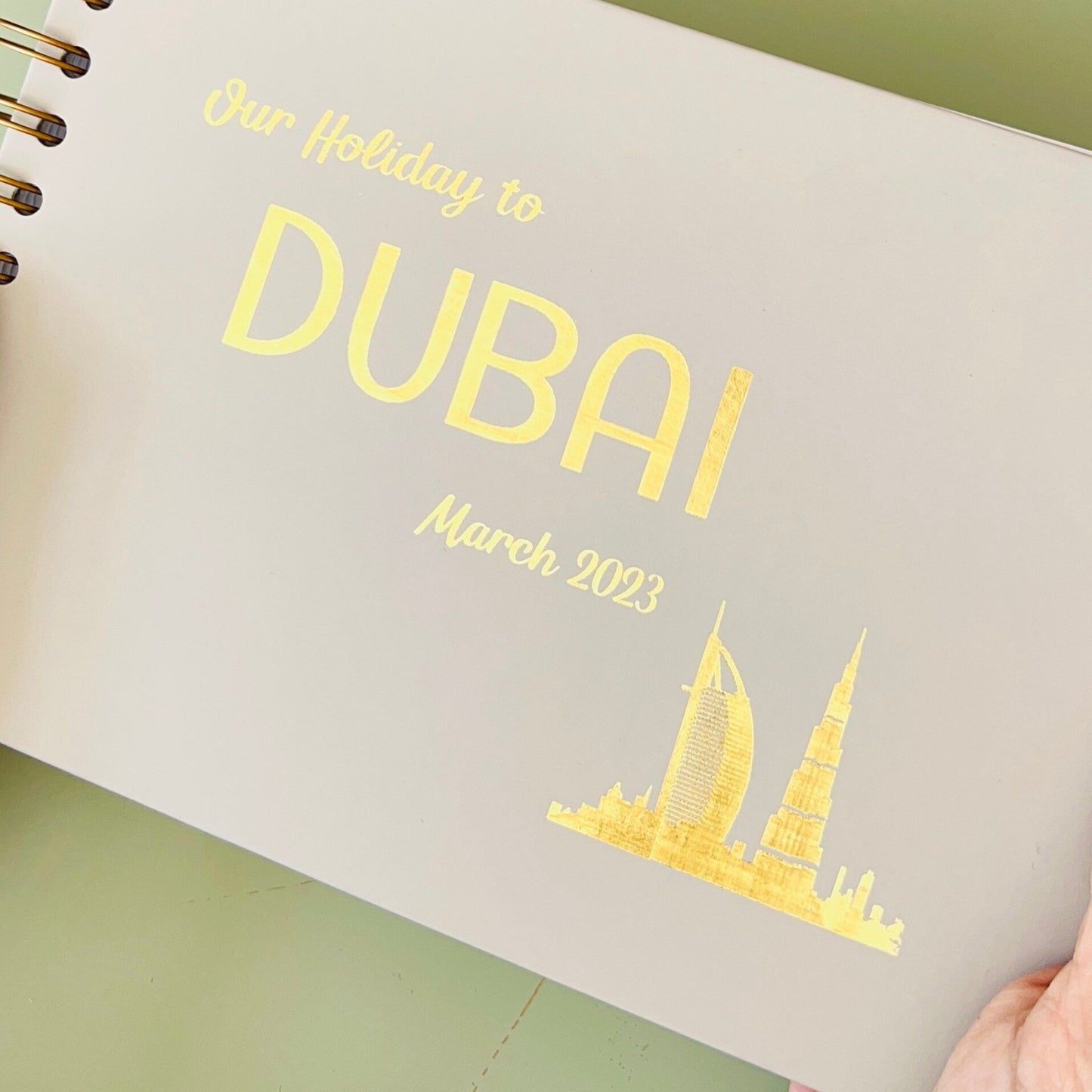 A5 hardback book in a stone colour that says Our Holiday to Dubai in gold foil and there are pictures of a holiday surrounding the book