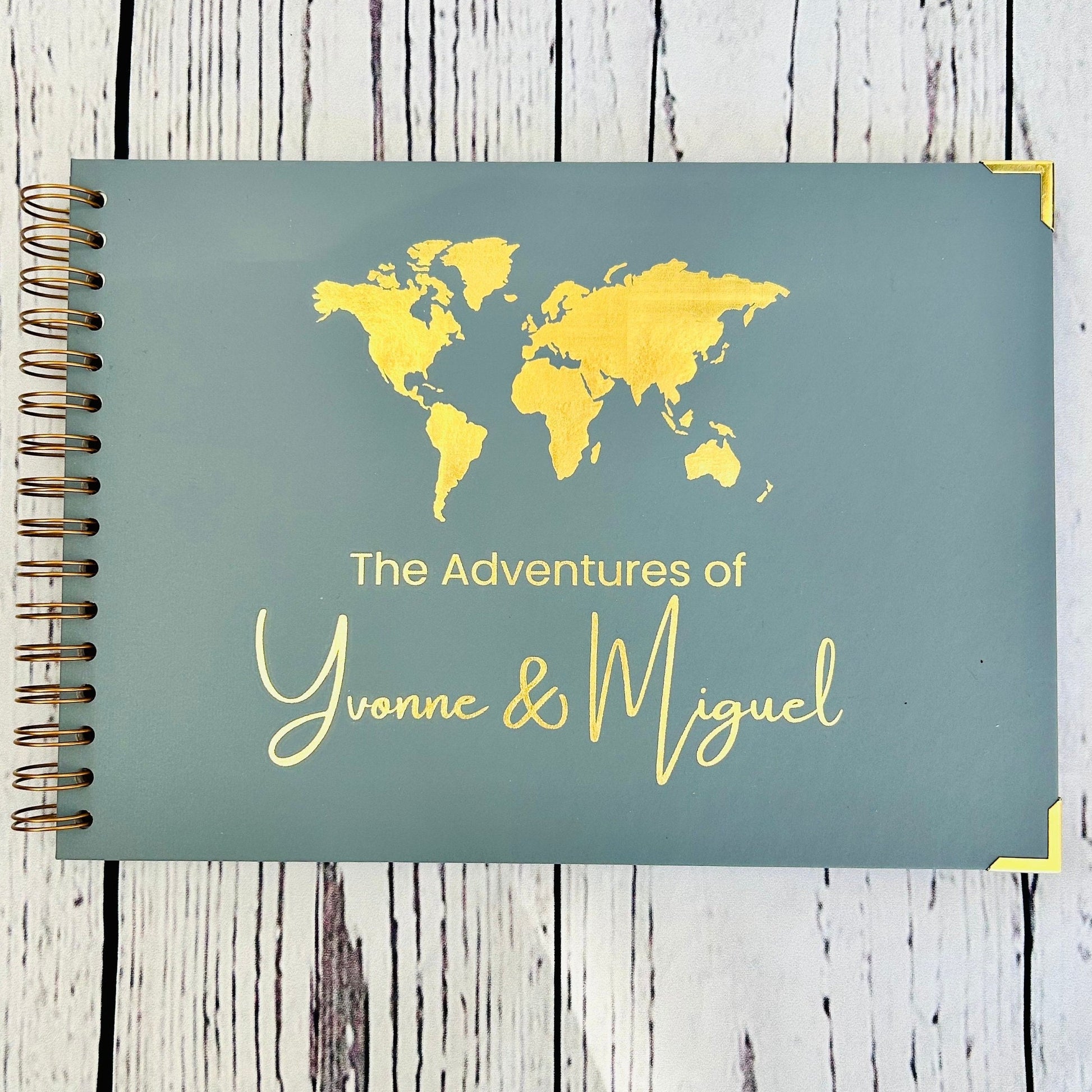 An A4 memory book in blue /grey with a map of the world and the words'The Adventures of Yvonne and Miguel' all in gold foil