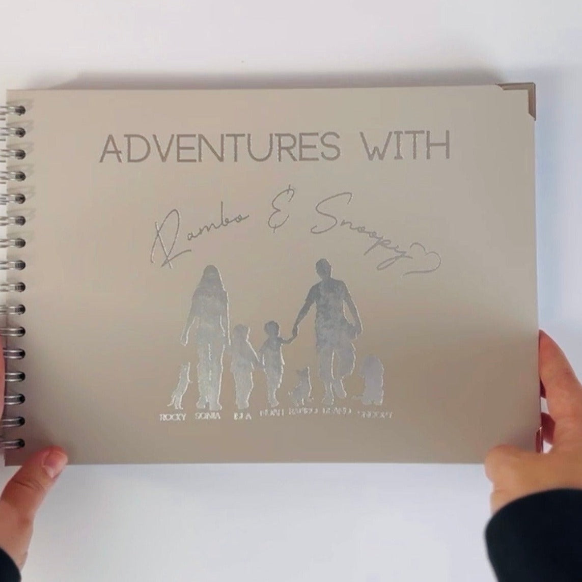 An A4 memory book in stone colour with the words 'Adventures with Rambo & Snoopy' and a silhouette of a family with two dogs walking with their names underneath each figure. All in silver foiling