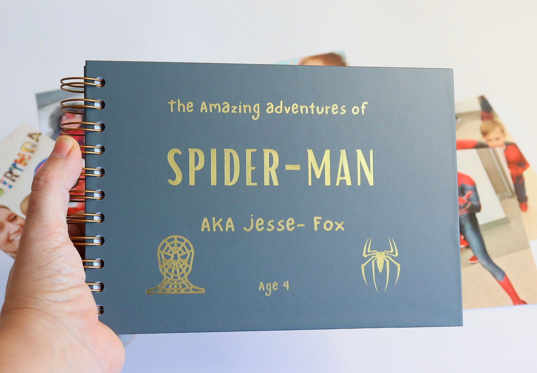 An A5 charcoal kids memory book which says 'The amazing adventures of Spiderman AKA Jesse-Fox' with two images of spiderman all in golf foil.