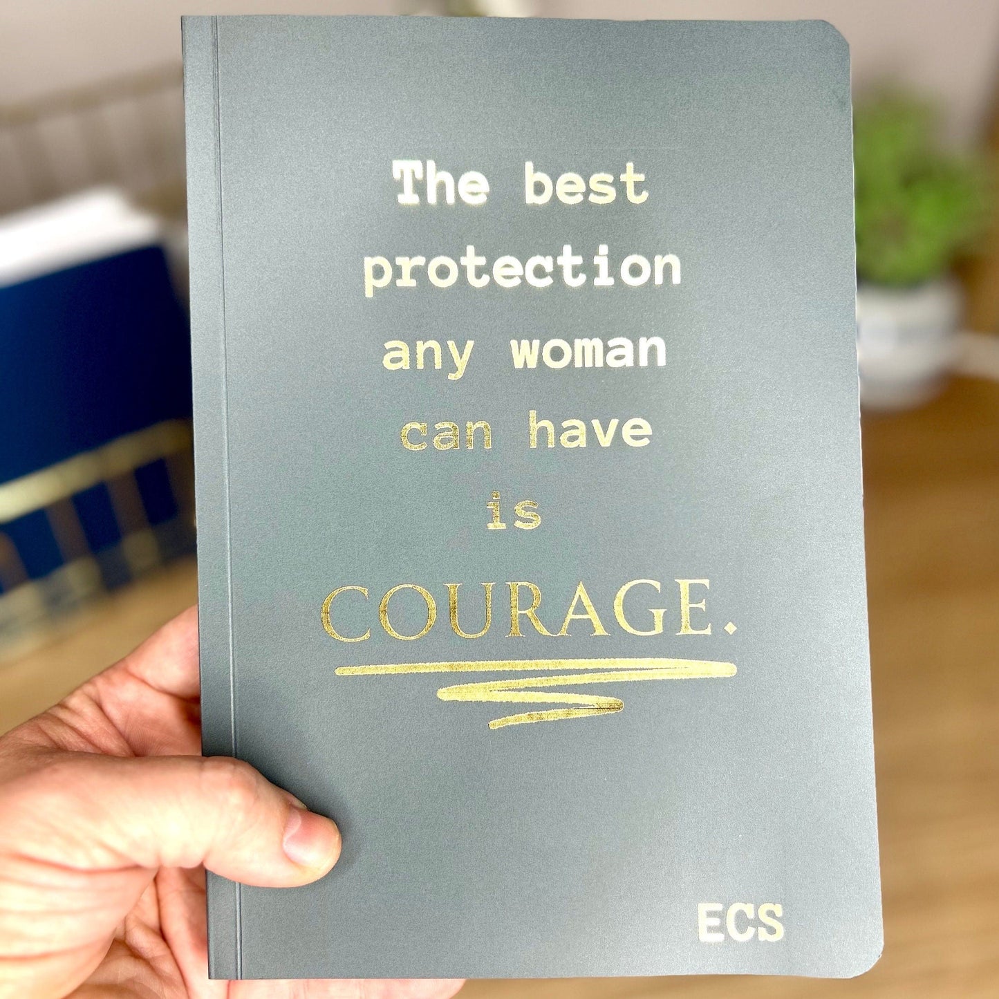 A charcoal softback notebook that says 'The best protection any woman can have is Courage' in golf foil