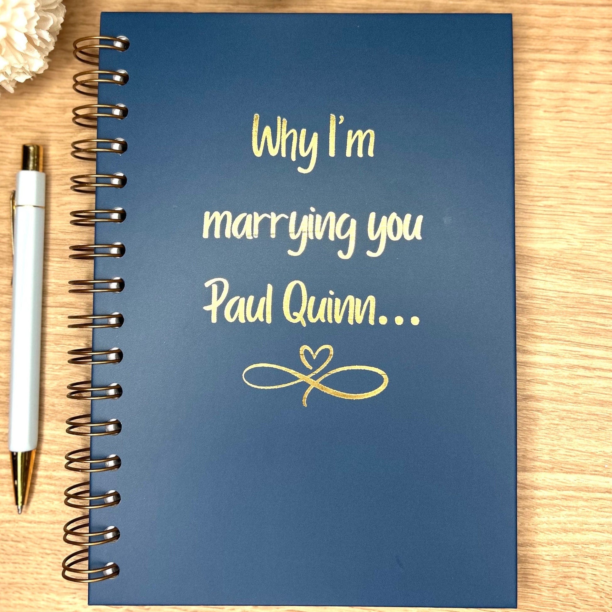 A hardback A5 notebook in midnight blue that says 'Why I'm marrying you Paul Quinn' in gold foil