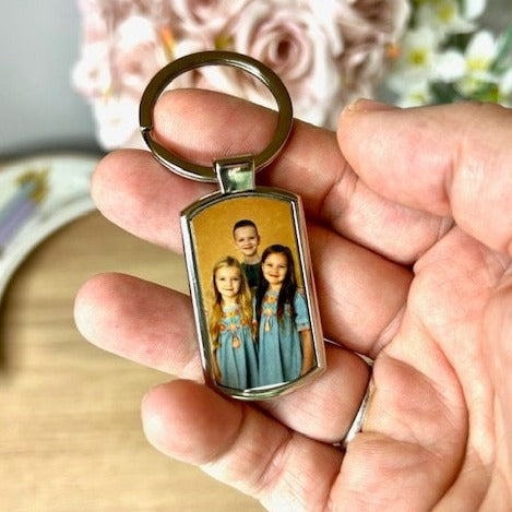 A 7.5cm x 2.5cm metal keyring with a large ring. The surface of the keyring has a pictures of three children smiling taking up the surface of the keyring