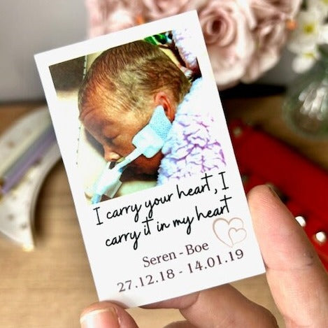 An 8x5 x 5x5 thin plastic card printed in a ploraid style with a picture of a small baby and the caption 'I carry you in my heart, Seren - boe' underneath