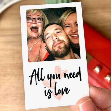 An 8x5 x 5x5 thin plastic card printed in a ploraid style with a picture of 3 happy people and the caption 'All you need is love' underneath
