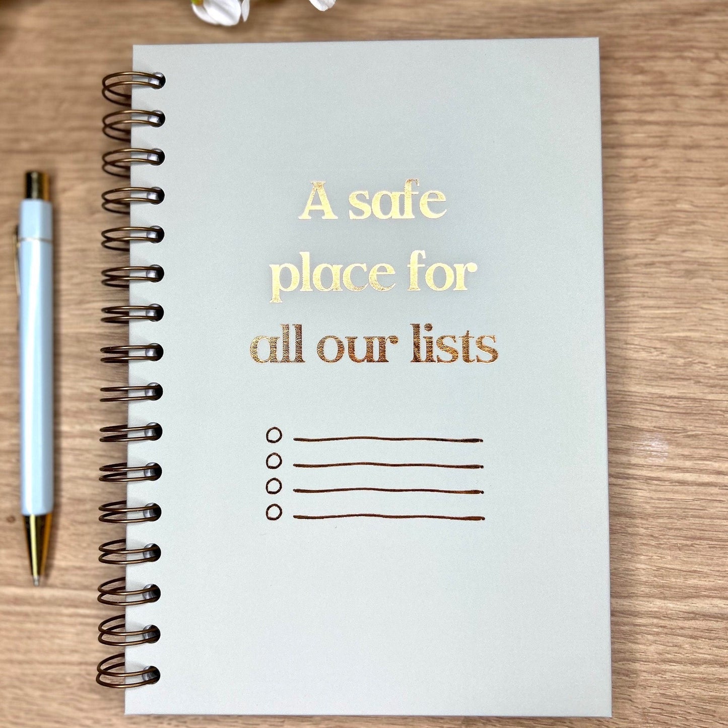 A hardback A5 notebook in light grey that says 'A safe place for all our lists' in bronze foil