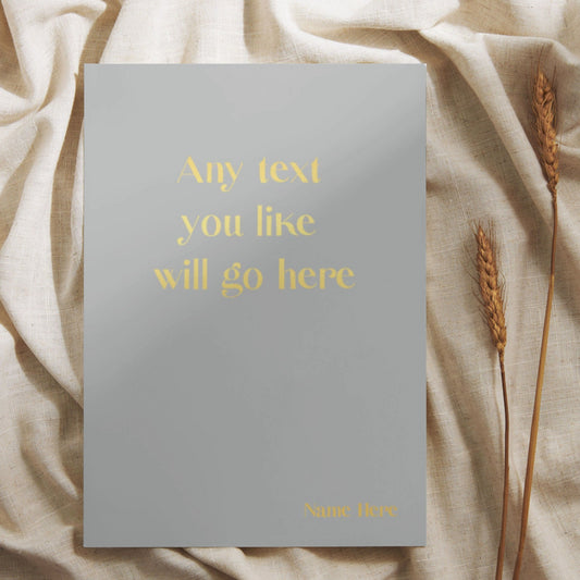 A light grey soft back notebook that says 'Any text you like will go here' in gold foil