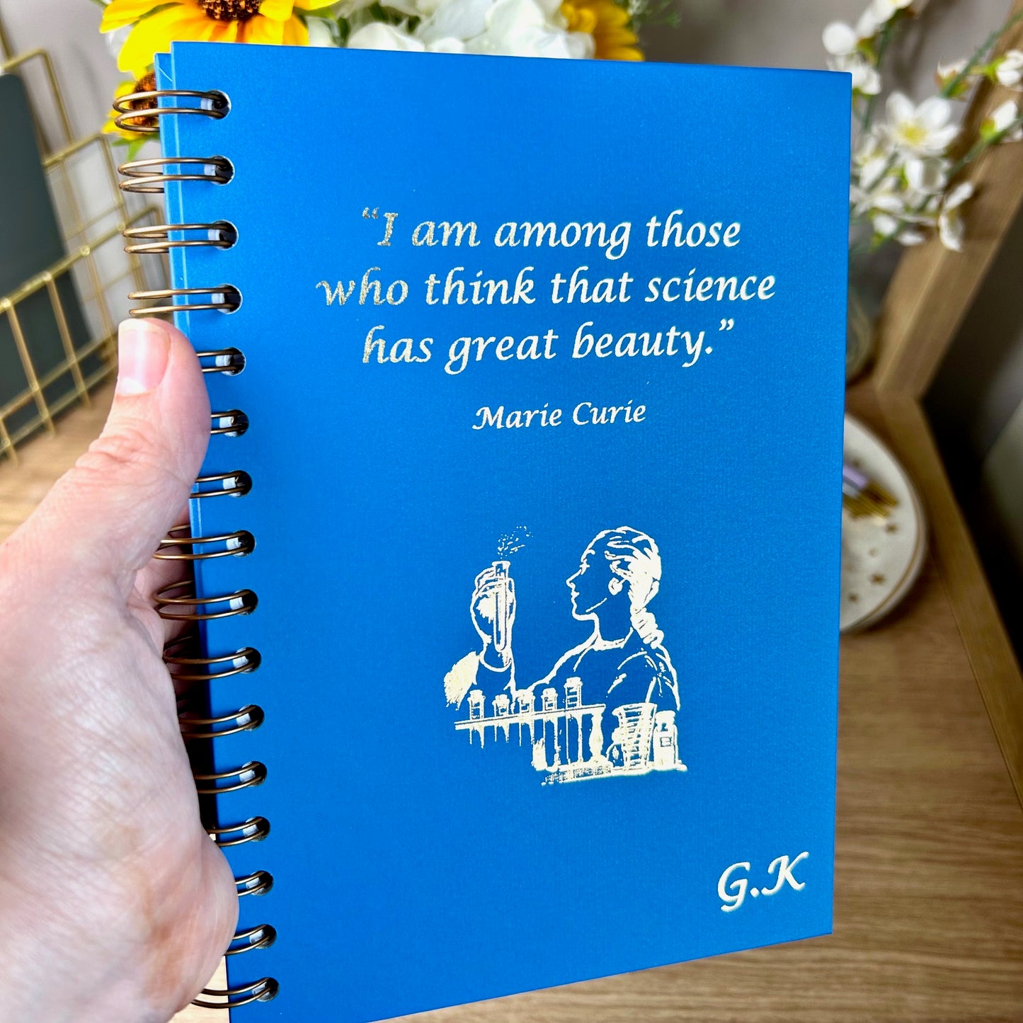 A hardback A5 notebook in Sea Blue that says 'I am among those who think that science has great beauty' with an image of a lady in a lab with test tube bottles, all in gold foil