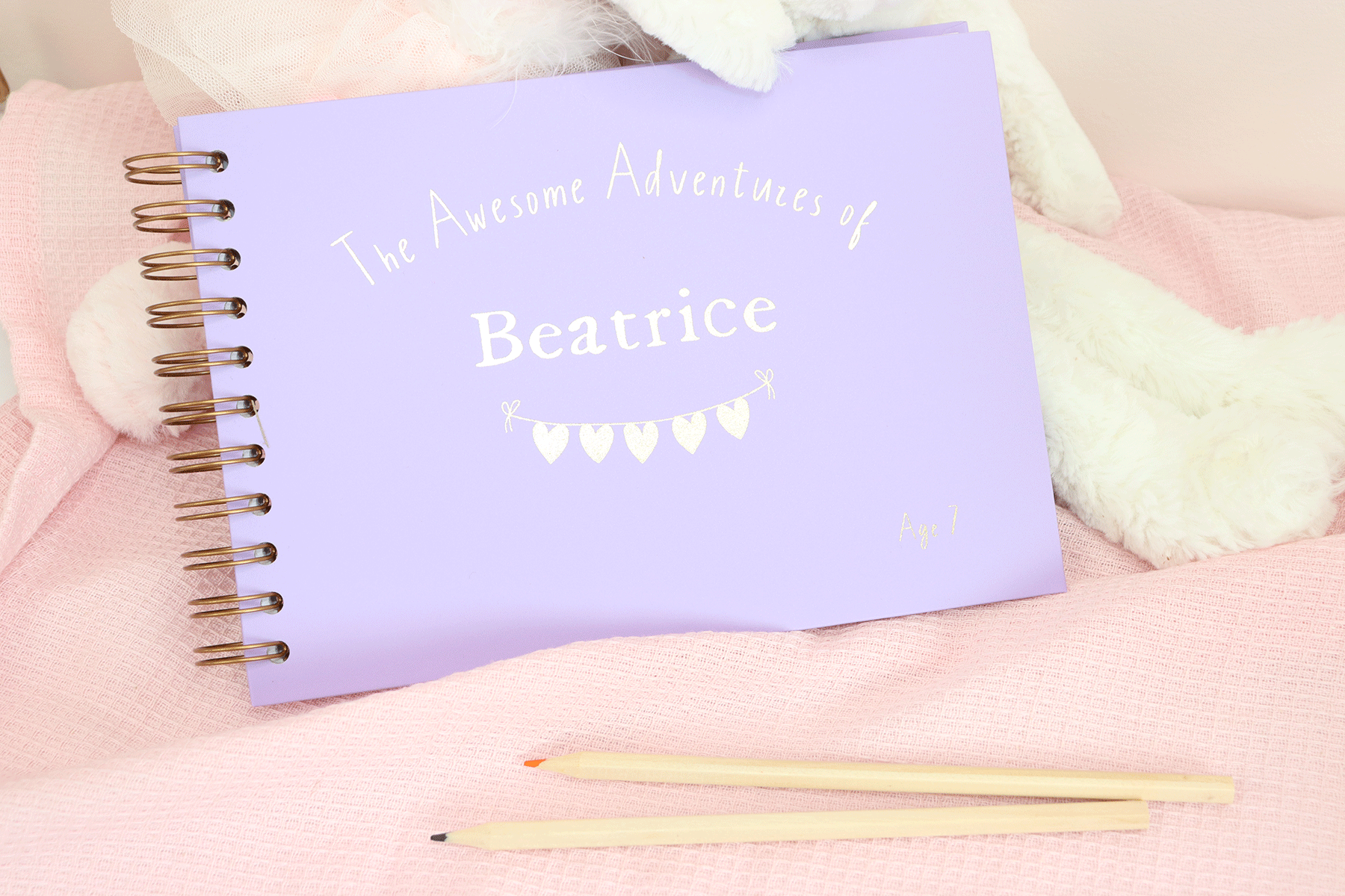 An A5 landscape lilac memory book, wire bound. The front cover reads 'the awesome adventures of Beatrice, Aged 7' in gold foiling. There are some gold love hearts on a banner