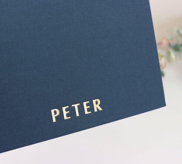 An up close image in detail of the gold embossed lettering on the navy blue notebook. the lettering reads PETER